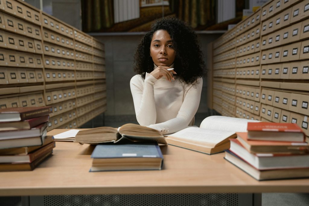 African American woman studying with books in a library archive area.